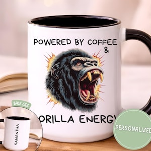 May include: White coffee mug with a black handle and interior. The mug features the text "POWERED BY COFFEE & GORILLA ENERGY" with a graphic of a roaring gorilla. A smaller mug with the name "SAMANTHA" is also visible.