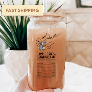May include: A glass bottle with a bamboo lid filled with a light brown liquid. The bottle has a label with the text "CAPRICORN" and "Nutrition Facts" with a graphic of the zodiac sign Capricorn. The label lists various personality traits and their corresponding percentage values.