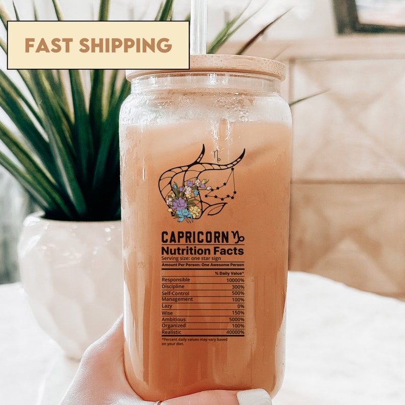 May include: A glass bottle with a bamboo lid filled with a light brown liquid. The bottle has a label with the text "CAPRICORN" and "Nutrition Facts" with a graphic of the zodiac sign Capricorn. The label lists various personality traits and their corresponding percentage values.