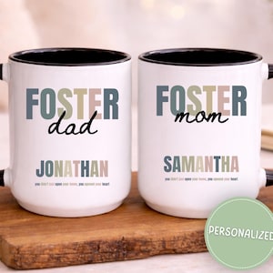 May include: Two white ceramic mugs with black handles and rims. One mug says "FOSTER dad" with the name "JONATHAN" below. The other says "FOSTER mom" with the name "SAMANTHA". Both mugs have a quote at the bottom.
