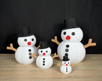 Könnte beinhalten: Vier weiße gestrickte Schneemänner mit schwarzen Zylindern und roten Nasen. Die Schneemänner sind in einer Reihe vom größten bis zum kleinsten angeordnet. Der größte Schneemann ist links und der kleinste rechts.