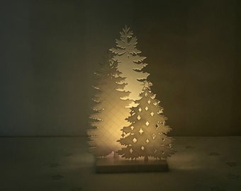 Könnte beinhalten: Eine weiße Holz-Weihnachtsbaumdekoration mit einem Licht im Inneren, das einen warmen Schein erzeugt. Der Baum besteht aus zwei Schichten, wobei die obere Schicht ein detaillierteres Design aufweist.