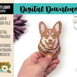 May include: A wooden cutout of a corgi dog's head with a floral pattern. The cutout is held in a hand and is ready to be used as a night light.