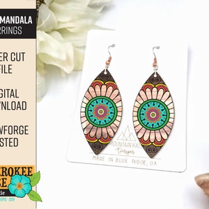 May include: A pair of laser cut wooden earrings with a daisy mandala design. The earrings are brown with pink, orange, yellow, green, blue, and white details. The earrings are on a white background with a white card that says "Mountain Kate Designs" and "Made in Blue Ridge, GA".