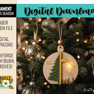 Puede incluir: Un adorno navide&ntilde;o redondo de madera con un pino verde en capas, una cruz amarilla y un recorte de estrella. El texto 'Tis the season' y 'Tis the reason' est&aacute; grabado junto a una silueta de un bel&eacute;n en la parte inferior.