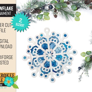 Op de afbeelding: Een lasergesneden sneeuwvlok ornamentbestand om digitaal te downloaden. De sneeuwvlok is wit met blauwe accenten en heeft een glas-in-lood look. Het bestand is getest voor Glowforge.