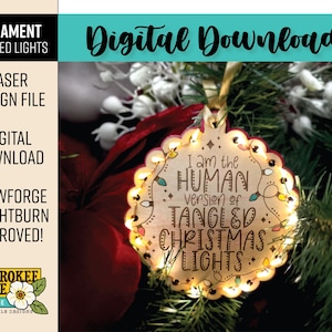 May include: A wooden Christmas ornament with a scalloped edge and the text "I am the HUMAN version of TANGLED CHRISTMAS LIGHTS." The ornament is illuminated with small lights and hangs on a Christmas tree.