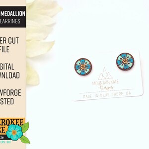 May include: A pair of laser cut wooden earrings featuring a blue and green floral design. The earrings are on a white background with text that reads "Mountain Kate Designs" and "Made in Blue Ridge, GA".