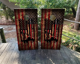 May include: Two wooden cornhole boards featuring a distressed American flag design and a silhouette of oil rigs. The boards are painted in red, white and blue.