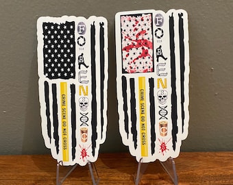 May include: Two black and white American flag stickers with yellow crime scene tape and the words "Crime Scene Do Not Cross" printed on them. The stickers also have the letters "FORENSIC" printed on them with various symbols.