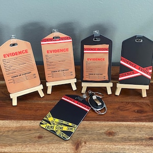 Puede incluir: Una colección de etiquetas de evidencia y llaveros. Las etiquetas son de color canela o negro con texto rojo que dice "EVIDENCE" y "CHAIN OF CUSTODY". Algunas etiquetas tienen cinta roja y blanca que dice "EVIDENCE". El llavero tiene cinta "CRIME SCENE".