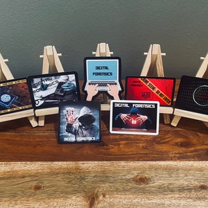 May include: Seven digital forensics stickers on small wooden easels. The stickers feature various designs, including a laptop, a hooded figure, and a crime scene tape. The text "DIGITAL FORENSICS" appears on each sticker.
