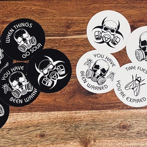 May include: Ten round stickers with black and white designs featuring skulls wearing gas masks and text. The text includes phrases like "Time Flies When You're Expired" and "When Things Go Sour".