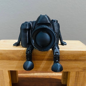 May include: A white ceramic mug with a black handle and the text "But First, Coffee" in a black, handwritten-style font. The mug is on a white surface.