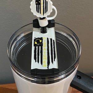 May include: White travel mug with a black handle and a black lid. The lid has a clear plastic top with a black ring around the edge. A black and white flag with the word "DISPATCHER" in yellow text is attached to the lid.