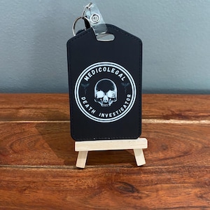 May include: Black key chain with a white circle containing a skull and the text "MEDICOLEGAL DEATH INVESTIGATOR".