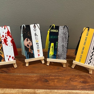 May include: Five different crime scene themed bookmarks displayed on small wooden easels. The bookmarks feature images of blood splatter, a skull, a fingerprint, a yellow crime scene tape, and a ruler.