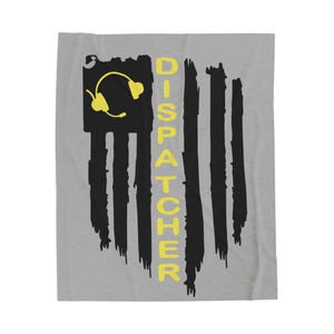 May include: A gray blanket with a distressed American flag design. The flag features black stripes and a yellow headset in the upper left corner. The word "DISPATCHER" is written vertically in yellow.