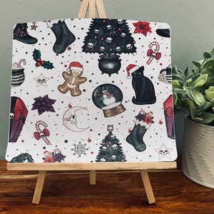 May include: A white background with a repeating pattern of Christmas and Halloween themed illustrations. The illustrations include a black cat, a gingerbread man, a skull and crossbones, a candy cane, a stocking, a Christmas tree, a snow globe, and a coffin.