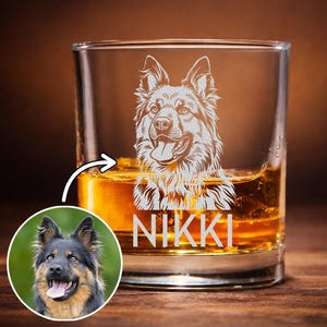 May include: A clear glass tumbler filled with amber liquid, featuring a white etched illustration of a long-haired dog and the name NIKKI printed below. A circular inset shows a photograph of the same dog with black and tan fur.