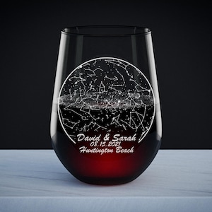 May include: A clear glass wine glass with a black and white star constellation design etched on the side. The design includes the text "David & Sarah 05.15.2021 Huntington Beach".