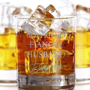 May include: A clear glass with a brown liquid and ice cubes. The glass has the words "Boyfriend - Fianc&eacute; - Husband Daddy" etched on the side.