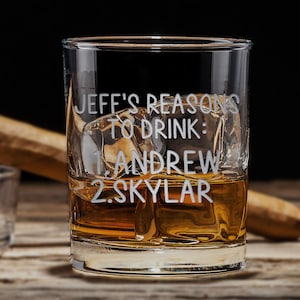 May include: A clear glass with a personalized inscription that reads "Jeff's Reasons to Drink: 1. Andrew 2. Skylar". The glass is filled with amber liquid and ice cubes.