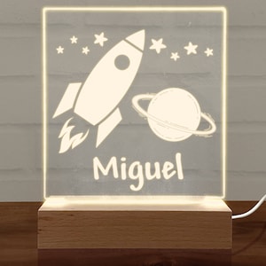 May include: A white acrylic night light with a rocket and planet design. The name "Miguel" is written below the design.