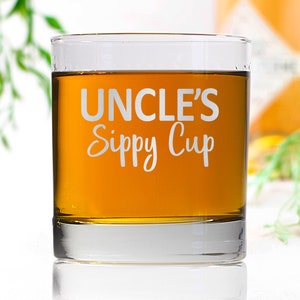 May include: A clear glass tumbler with the text "UNCLE'S Sippy Cup" etched on the side. The glass is filled with a light amber liquid.