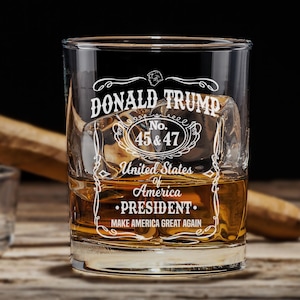 May include: A clear glass whiskey tumbler with a white design that says "DONALD TRUMP No. 45 & 47 United States of America •PRESIDENT. MAKE AMERICA GREAT AGAIN".