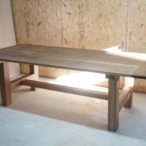 May include: A long, rectangular wooden table with a simple, modern design. The table has a light brown finish and a natural wood grain. The table is supported by four sturdy legs and a single stretcher.