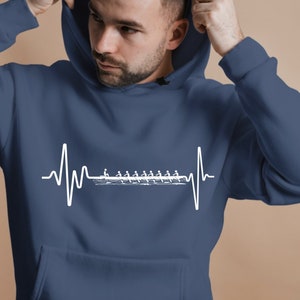 Peut inclure: Un sweat à capuche bleu marine avec un graphique de battement de cœur blanc représentant un équipage d'aviron. Le graphique montre une rangée de rameurs dans un bateau avec des rames.