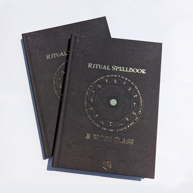 Op de afbeelding: Twee bruine, in leer gebonden boeken met gouden letters. Het bovenste boek heeft de titel "Ritual Spellbook" en de tekst "Witch Class". Het onderste boek heeft de tekst "Ritual" zichtbaar.