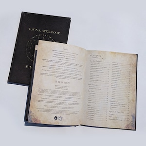 Op de afbeelding: Open boek met een zwarte leren kaft en gouden letters. De titel is "Ritual Spellbook". Het boek is open op een pagina met een inhoudsopgave met een lijst van verschillende spreuken en rituelen.