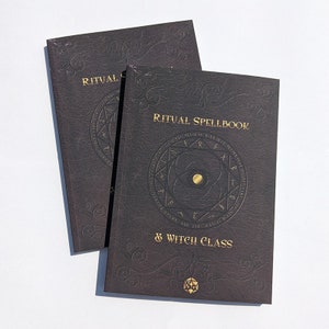 Op de afbeelding: Twee zwarte, in leer gebonden boeken met gouden letters. Het bovenste boek zegt "Ritual Spellbook & Witch Class". Het onderste boek zegt "Ritual". Beide boeken hebben een gouden cirkel met runen en een gouden vijfpuntige ster.