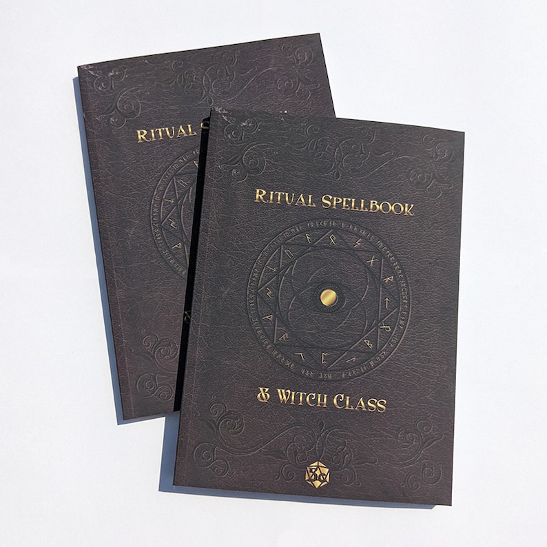 Op de afbeelding: Twee zwarte, in leer gebonden boeken met gouden letters. Het bovenste boek zegt "Ritual Spellbook & Witch Class". Het onderste boek zegt "Ritual". Beide boeken hebben een gouden cirkel met runen en een gouden vijfpuntige ster.