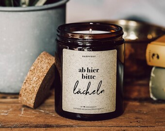 May include: A brown glass candle jar with a cork lid. The label reads "HappySoy" and "ab hier bitte lächeln". The candle is handmade with natural soy wax.