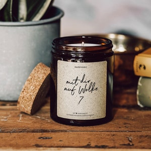 May include: A brown glass candle jar with a cork lid. The label reads "HappySoy" and "mit dir auf Wolke 7" with a heart symbol. The candle is made with natural soy wax.