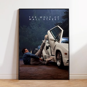 Peut inclure: Affiche encadrée du film "Le Loup de Wall Street". L'image montre une voiture de sport blanche avec une portière ouverte et une personne en chemise bleue et pantalon gris. Le titre est en haut.