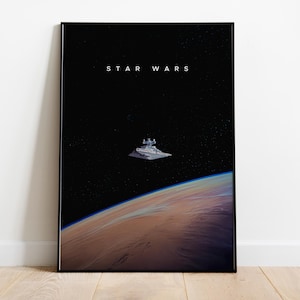 Puede incluir: Una impresión artística enmarcada de Star Wars. El fondo negro presenta el texto "STAR WARS", una nave espacial y el horizonte de un planeta. La impresión se muestra sobre un suelo de madera.