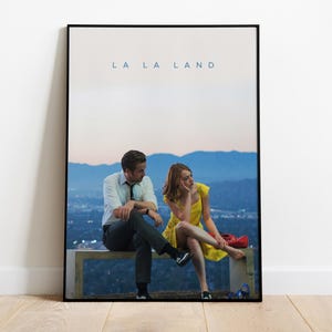 Puede incluir: Un póster de película para la película "La La Land" con un hombre y una mujer sentados en un banco con vistas a una ciudad. El póster tiene un fondo degradado azul y rosa.