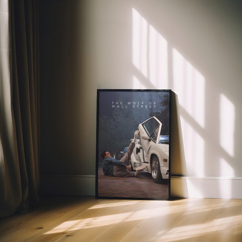 May include: A framed poster of a scene from "The Wolf of Wall Street." The image depicts a white sports car with an open door and a person in a suit. The poster is propped against a white wall, with the text "THE WOLF OF WALL STREET" at the top.