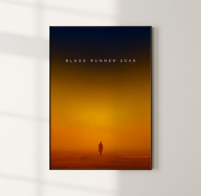 May include: A minimalist poster with a black frame and a gradient background that transitions from dark blue to orange. The text "BLADE RUNNER 2049" is centered in white at the top of the poster. A silhouette of a person walking away from the viewer is in the center of the poster.