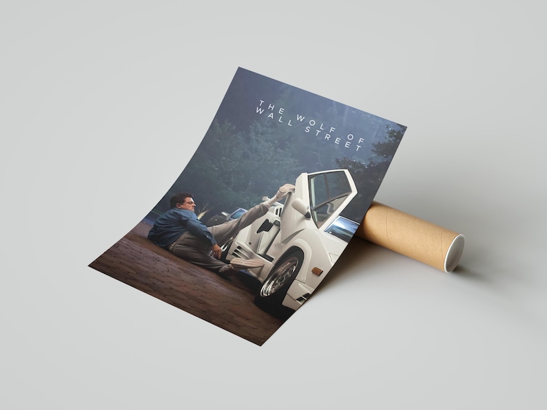 May include: Poster print of a scene from "The Wolf of Wall Street" with a white sports car and a man in a blue jacket. The title is printed at the top. The poster is rolled and placed next to a cardboard tube.
