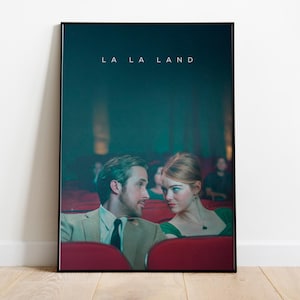 Puede incluir: Un póster enmarcado de la película "La La Land" que muestra a un hombre y una mujer en un cine. El hombre lleva un traje y corbata, y la mujer un vestido verde. El póster está en un marco negro y se exhibe en una pared blanca.