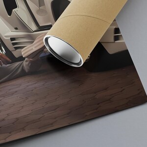 May include: A rolled poster with a brown outer layer and a silver inner layer, positioned on a brown, textured surface. The poster is angled towards a white car with a person in the background.
