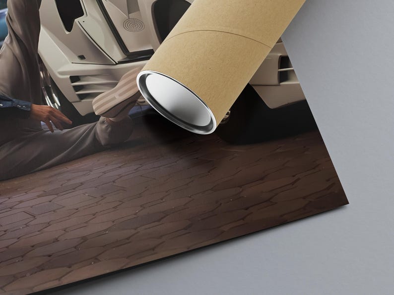 May include: A rolled poster with a brown outer layer and a silver inner layer, positioned on a brown, textured surface. The poster is angled towards a white car with a person in the background.