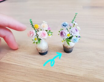 May include: Two miniature flower arrangements in ceramic pots. The arrangement on the left has pink, white, and yellow flowers. The arrangement on the right has purple, white, and blue flowers.