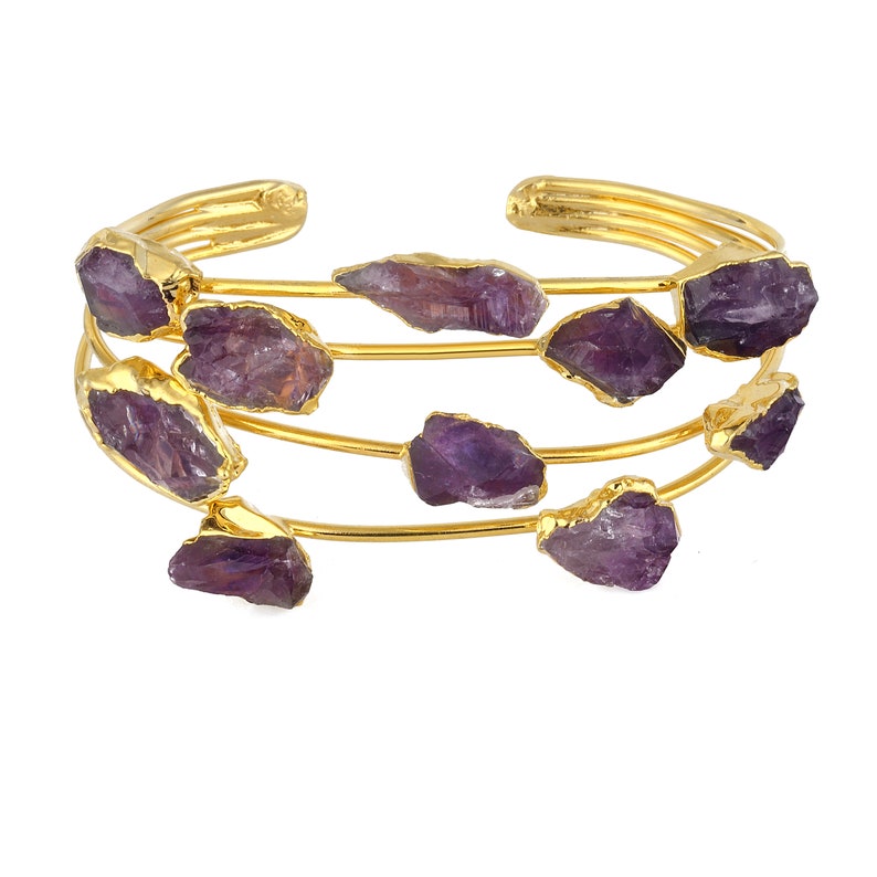 May include: Gold bangle bracelet with multiple rows of amethyst gemstones. The bracelet is made of thin gold wire and features several amethyst stones of varying sizes and shapes.