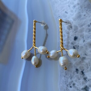 May include: A pair of gold earrings with a twisted wire design and multiple pearl drops.